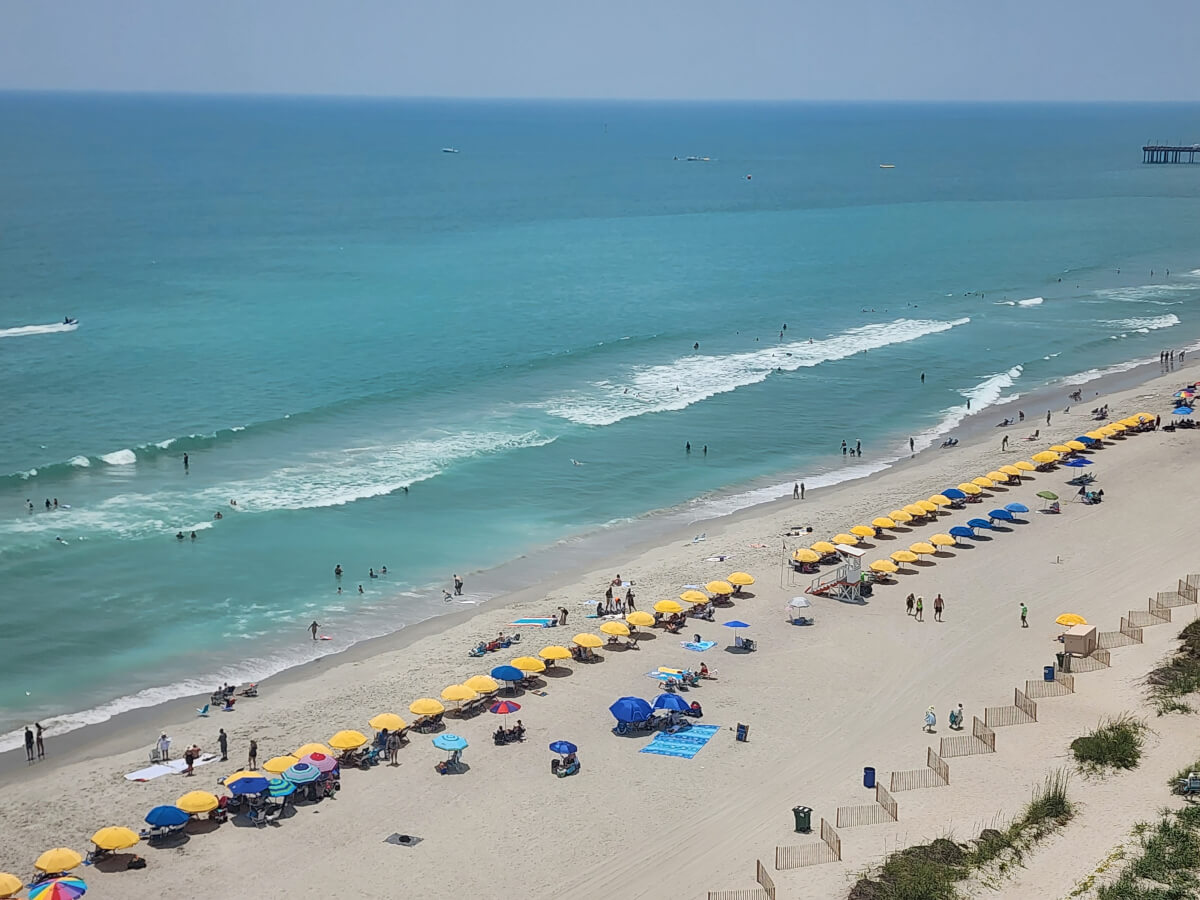 Aerial view of Myrtle Beach's blue waters with rows of yellow beach umbrellas and sunbathers.