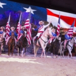 People on horses stand in a line, all holding American flags.